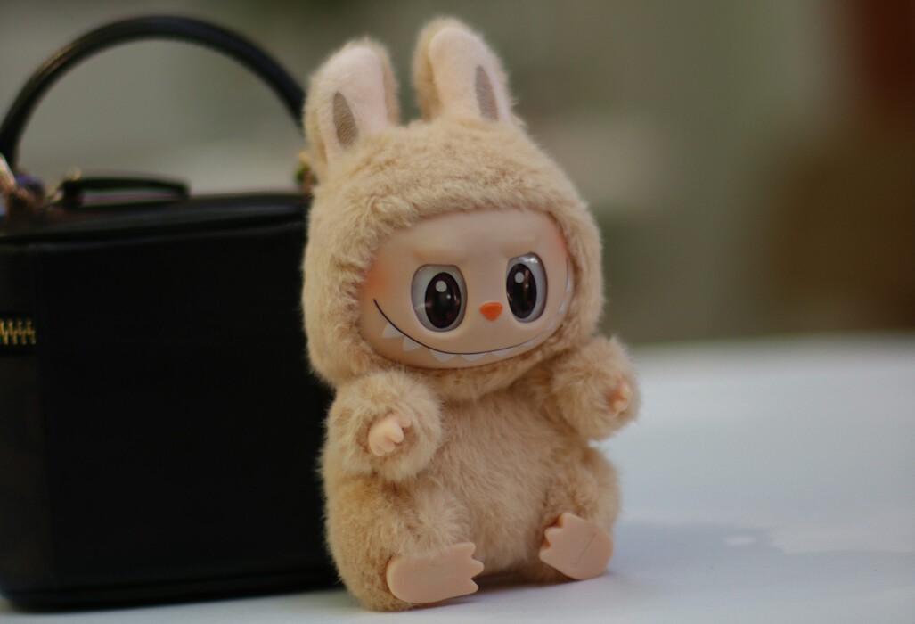 Peluche de Labubu, un animal en forme de lapin posée sur une table contre un sac